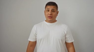 Genç İspanyol adam gülümseyip kendini işaret ederken parmaklarıyla izole edilmiş beyaz arka plan duvarına işaret ediyor.