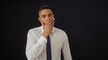 Esneyen ve esneyen İspanyol bir adam, beyaz gömlek ve kravat giyiyor, siyah bir arka planda izole edilmiş..