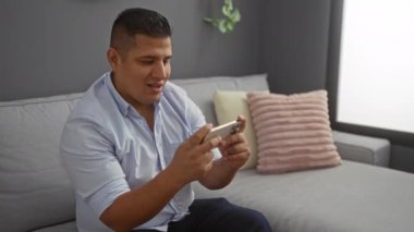 Genç adam, modern dekorla rahat bir evde otururken telefonuyla oyun oynuyordu.