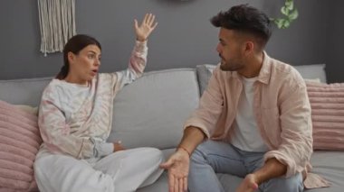 Kadın ve erkek rahat oturma odasında pembe yastıklar ve gri duvarlarla konuşuyor.