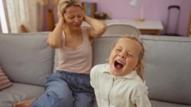 Anne ve kızı evde çocuk bağırırken kadın oturma odasındaki bir kanepede otururken kulaklarını kapatıyor.