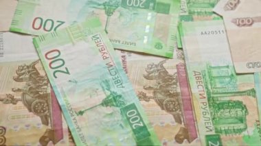 Rus rublesi banknotlar düz bir yüzeye saçılmış canlı yeşil ve kırmızı tonlarda çeşitli mezhepler sergiliyor, para biriminin karmaşık tasarımları ve ayrıntılarını vurguluyor..