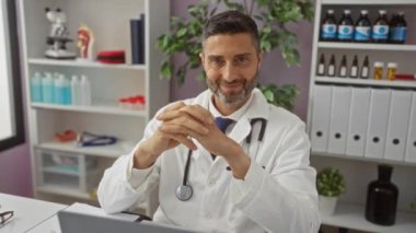 Hastane ofisinde gülümseyen doktor beyaz önlüklü ve steteskoplu tıbbi malzemeler ve arka planda bitkilerle..