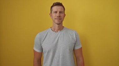 Gri gömlekli genç adam, neşeli bir şekilde dilini parlak sarı bir arka plana doğru uzatıyor, eğlence ve cazibe hissi yayıyor, canlı bir portre sahnesi yaratıyor..