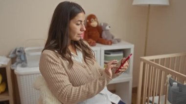 Yatak odasında oyuncak ve beşiğiyle akıllı telefon kullanan bir kadın, sakin ve besleyici bir atmosfer yayıyor..