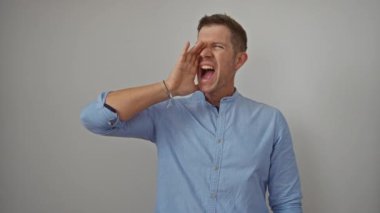 Düz beyaz bir arkaplana karşı enerjik bir şekilde bağıran bir adam. Sıradan mavi bir gömlek giyen, etkileyici el hareketleriyle coşkulu duygular ve coşku gösteren bir adam..