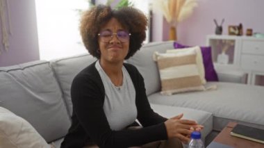 Kıvırcık saçlı bir kadın, hoş bir oturma odasında oturmuş, kötü bir koku yüzünden burnunu kapatıyor, hoşnutsuz bir ifade sergiliyor ve modern dekorasyonla çevrili..