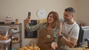 Kadın ve erkek bir fırında birlikte çalışıyor, gülümsüyor ve selfie çekiyorlar etrafları hamur işleri ve fırınlarla çevriliyken..
