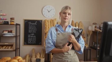 Fırında elinde ekmek ve hamur işleri olan bir pano tutan genç bir kadın.