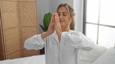 Huzurlu bir yatak odasında, yatakta meditasyon yapan, kapalı gözlü rahat pijamalar giyen, sabah sükunetinin keyfini çıkaran ve kapalı alandaki farkındalığı kucaklayan bir kadın..