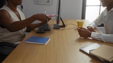 Ofiste masa, bilgisayar ve not defterleri olan, gülümseyen ve profesyonel iş ortamında meşgul olan bir adama belge veren bir kadın.