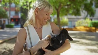 Güneşli bir günde şehir parkında elinde chihuahua köpeği tutan orta yaşlı bir kadın.