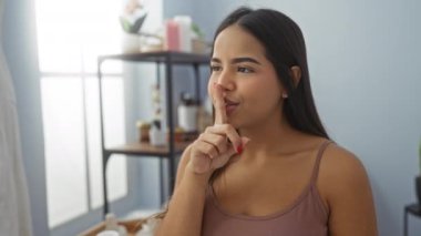 Esmer saçlı bir kadın sessiz kalmak için modern dekorlu sakin bir spa odasında el kol hareketi yapıyor. Huzurlu güzellik merkezinde rahatlama ve sağlığa işaret ediyor..