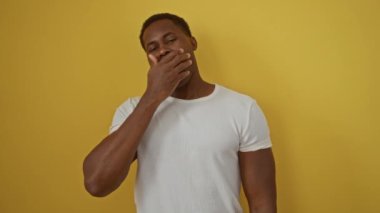 Adam esniyor ve esniyor, canlı sarı bir arka plana karşı, sabah rutinini ifade ediyor, beyaz bir gömlek içinde, rahatlatıcı enerji taşıyor ve uyanma modunda..