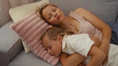Anne ve kızı rahat bir kanepede birlikte uyuyorlar, aile bağlarını oturma odasında sergiliyorlar.