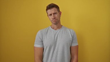 Parlak sarı bir duvarın önünde poz veren genç bir adam. Gri bir tişört giyiyor. Kendine güvenen bir ifadesi var..