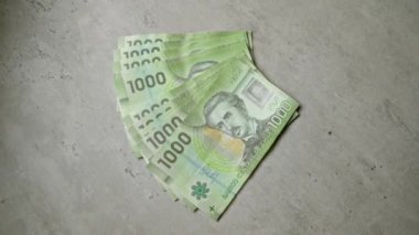 Şili banknotları, farklı detaylar ve canlı renkler gösteren birden fazla 1000 peso banknotla beton bir yüzey üzerine kuruludur.