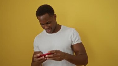 Sarı arka planda video oyunu oynayan genç adam, beyaz tişört giyiyor, gülümsüyor, odaklanıyor, eğleniyor, izole edilmiş, rahat, modern, yaşam tarzı.