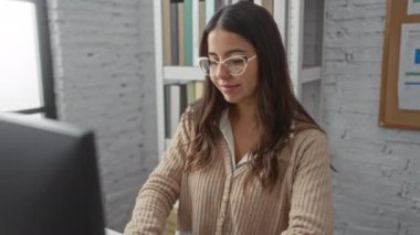 Modern bir ofiste çalışan bir kadın, genç ve çekici bir esmer, gözlüklü, kitap rafları ve şık bir iç duvar ile çevrili..