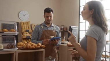 Kadın ve erkek, pastanede içeride sergilenen ekmek ve hamur işleriyle etkileşim halindeler.