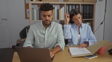 Erkek ve kadın bir ofiste birlikte çalışıyor, belgelere ve laptopa odaklanıyor, iş ortaklığı ve profesyonel takım çalışması sergiliyor.