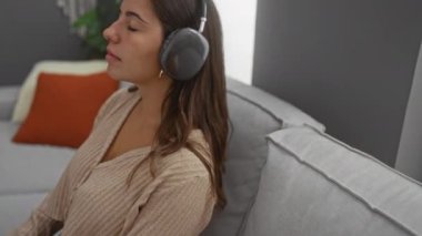 Oturma odasındaki rahat koltukta kulaklıkla dinlenen, çiçekli ve yastıklı bir kadın, müzikle eğlenen ya da huzur dolu ev ortamında meditasyon yapan, gözleri kapalı ve dingin bir kadın..