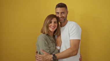 Sarı bir arka plana karşı sevgi dolu bir kucaklaşma içinde gülümseyen çift.