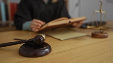 Masasında tokmak ve teraziyle mahkeme salonunda kitap okuyan bir kadın.