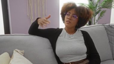 Oturma odasındaki koltukta otururken elini serinleten bir kadın. Kapalı salonda bitkiler ve modern dekorlarla. Yaz boyunca sıcak bir ortam..