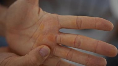 Yetişkin bir adam koyu arkaplan üzerinde elleri yakından inceliyor. Sıkı çalışma ve ağır işçiliği temsil ediyor..