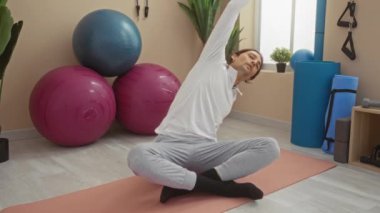 Spor salonundaki yoga minderinin üzerinde egzersiz topları ve bitkilerle uzanan genç adam.