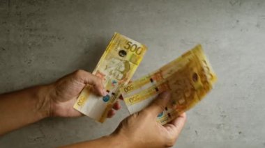 Somut bir arka planda Filipinli pezo banknotlarını sayan eller, Filipinli parasal işlemleri ve günlük finansal faaliyetlerde para akışını vurguluyor.