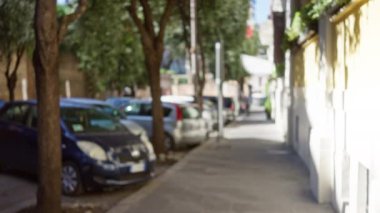 Roma 'da bulanık bir sokak sahnesi. Odaklanmış arabaları gösteriyor. Ağaçlar ve kaldırımlar güneşli bir şehir ortamında..