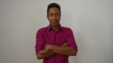 Genç adam izole edilmiş beyaz bir arka plana karşı güvenle gülümsüyor kolları çaprazlanmış bir şekilde cazibesini ve tarzını gösteriyor, canlı bir gömlek giyiyor, çekici yetişkin erkek özelliklerini vurguluyor..