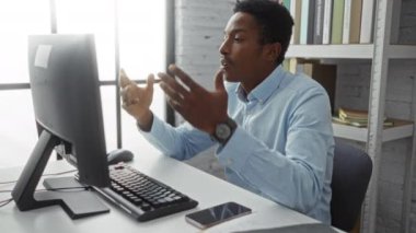 Ofiste, raflar ve kağıtlarla çevrili bir video konferansı düzenleyen genç adam, profesyonel bir iç mekan olduğunu vurguluyor..