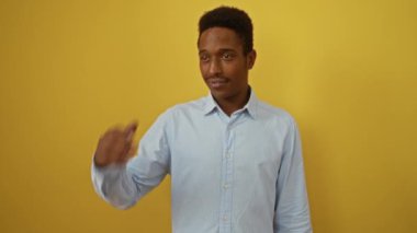 Genç Afro-Amerikalı adam tişörtünü giyip uzaklara bakıyor, mutlu ve gülümsüyor, izole edilmiş sarı arka planı araştırıyor.