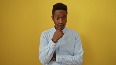 Sarı arka planda gömlek giyen Afro-Amerikalı genç bir adam dramatik bir ifadeyle başını silah gibi gösteren parmaklarıyla jest yapıyor.