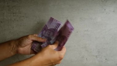 Endonezyalı el, somut arka plana karşı rupiah parası sayıyor. Finans kavramını gösteriyor.