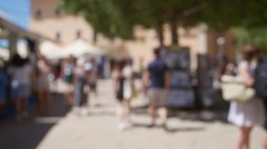 Mallorca 'da güneşli bir sokakta bulanık arka plan ve bokeh etkisi ile yürüyen, yaz kıyafetleri içinde erkek ve kadınları gösteren odaksız insanlar..