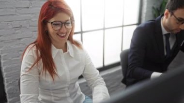 İki iş adamı, bir kadın ve bir erkek, ortak bir toplantı sırasında bir ofiste gülümsüyor ve bilgisayarlar üzerinde çalışıyorlar..