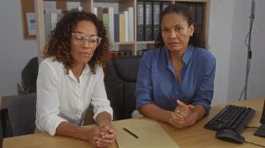 Düzenli bir iş yerindeki klasörlerle dolu ofis masasında iş tartışan iki kadın.