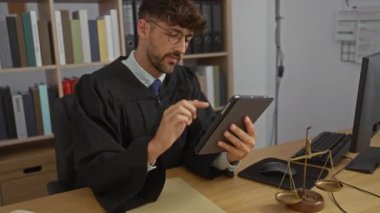 Genç yargıç, adalet terazisiyle büro masasında tablet kullanıyor.