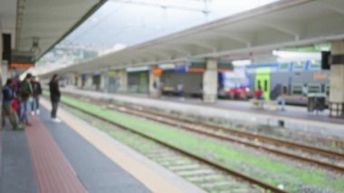 Bir grup insan bulanık bir şehir tren istasyonunda bekliyor. Yoğun bir metropol tren yolu sahnesi sergileniyor..