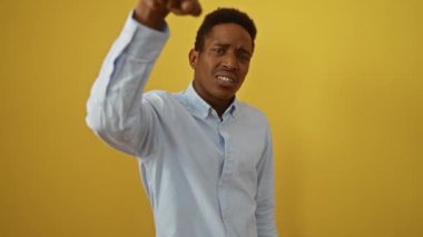Genç, Afro-Amerikan gömlekli adam öfkeli ve kızgın bir şekilde, izole edilmiş sarı arka planda, hoşnutsuz ve hayal kırıklığına uğramış kamera ifadesinden dolayı seni suçluyor.