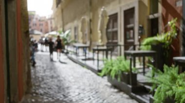 Bulanık suretler, Roma 'nın eski kasabasındaki bitkiler ve tarihi binalarla aydınlık bir kaldırım taşı caddesinde yürür ve hayaller kuran, zamansız bir atmosfer yaratır..