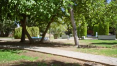 Yeşil ağaçlar, patika ve açık hava kentsel manzarası bulanık efekt ve doğal güneş ışığıyla yakalanmış, sakin ve huzurlu bir çevreyi çağrıştırıyor..