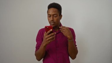 İzole edilmiş beyaz arka planda akıllı telefon kullanan, canlı bir gömlek giyen, teknoloji ve yaşam tarzı temaları için uygun merak ve odaklanma sergileyen bir adam..