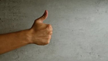 Gri beton arka plana karşı olumlu bir hareket sergileyen adam pozitifliği ve onayını vurguluyor..