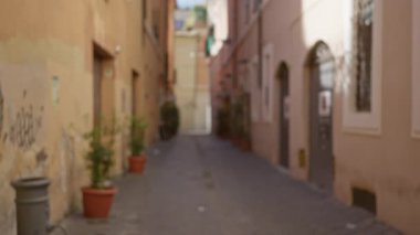 Roma, İtalya 'da eski bir kasaba caddesinin bulanık manzarası. Bokeh etkisi ve kaldırım taşlarının olduğu yerde saksı bitkileri var..