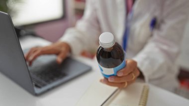 Eczanede dizüstü bilgisayar üzerinde çalışırken ilaç şişesini inceleyen kadın eczacı.